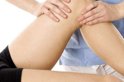 Fisioterapeuta aplicando massagem na coxa e joelho de um paciente para reabilitação e liberação muscular.