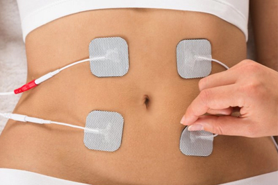 Mulher recebendo tratamento de eletroestimulação com eletrodos no abdômen para tonificação muscular e estética corporal.