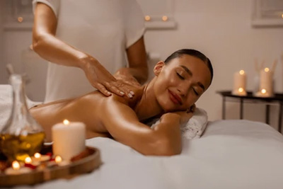 Mulher sorrindo de olhos fechados enquanto recebe uma massagem relaxante nas costas em um spa de luxo à luz de velas.