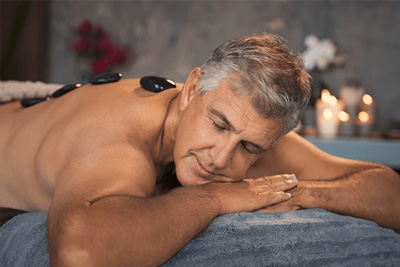 Homem maduro de cabelos grisalhos relaxando enquanto recebe uma massagem com pedras quentes nas costas em um spa.