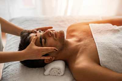 Homem deitado de costas recebendo uma massagem facial relaxante para alívio de tensão na mandíbula e no rosto.