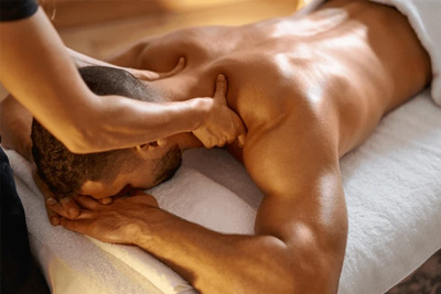 Massoterapeuta aplicando massagem de ponto-gatilho no ombro de um homem para liberação miofascial e alívio de dor.