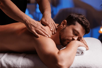 Homem com barba recebendo uma massagem desportiva nos ombros para liberação de tensão muscular em um ambiente relaxante.