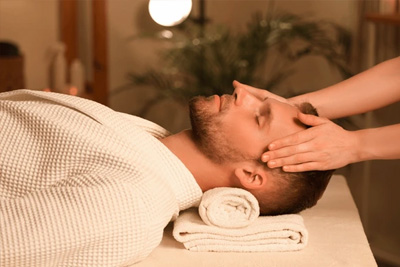 Homem de roupão recebendo uma massagem relaxante na cabeça (craniana) para alívio de estresse em um spa.