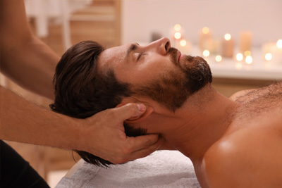 Homem relaxando enquanto recebe uma massagem no pescoço e na cervical em um spa à luz de velas.