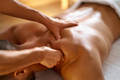 Massoterapeuta aplicando massagem de ponto-gatilho no ombro de um homem para liberação miofascial e alívio de dor.