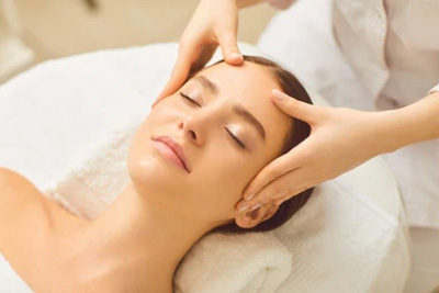Mulher de olhos fechados recebendo uma massagem facial relaxante para alívio de estresse e rejuvenescimento da pele.
