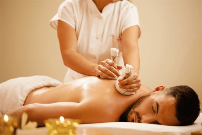 Homem relaxado recebendo uma massagem com pindas chinesas quentes nas costas para alívio de estresse e dores.