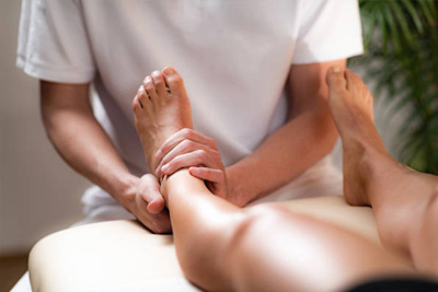 Terapeuta aplicando massagem no pé e tornozelo de um cliente para alívio de dor e relaxamento.