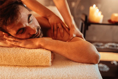 Homem relaxando profundamente enquanto recebe uma massagem nos ombros em um spa à luz de velas.