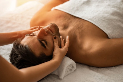 Homem deitado de costas recebendo uma massagem facial relaxante para alívio de tensão na mandíbula e no rosto.