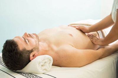 Homem relaxado recebendo uma massagem abdominal para bem-estar e melhora da digestão em uma clínica de estética.